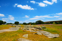 photo of meadow with large fieldstones and trees in the distance under a blue sky