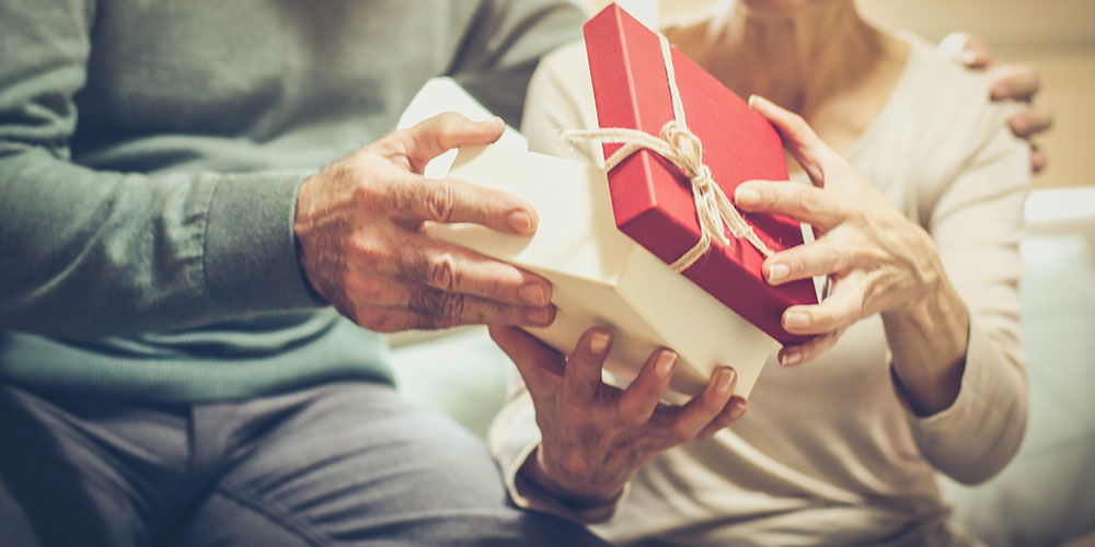 Two elderly people, their faces out of frame, jointly holding an unopened gift that is tied with a bow.