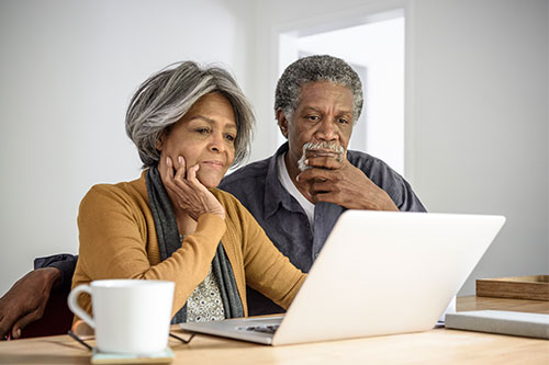 Two elder people sitting at table and looking at a laptop computer.