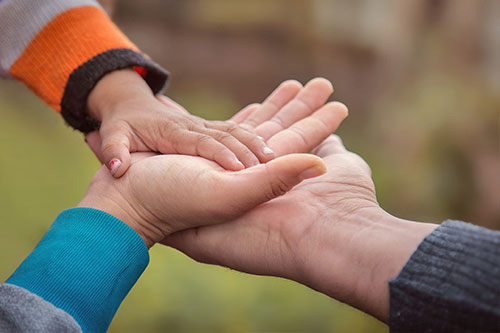 Three hands resting on top of each other, one large, one medium, and one small.